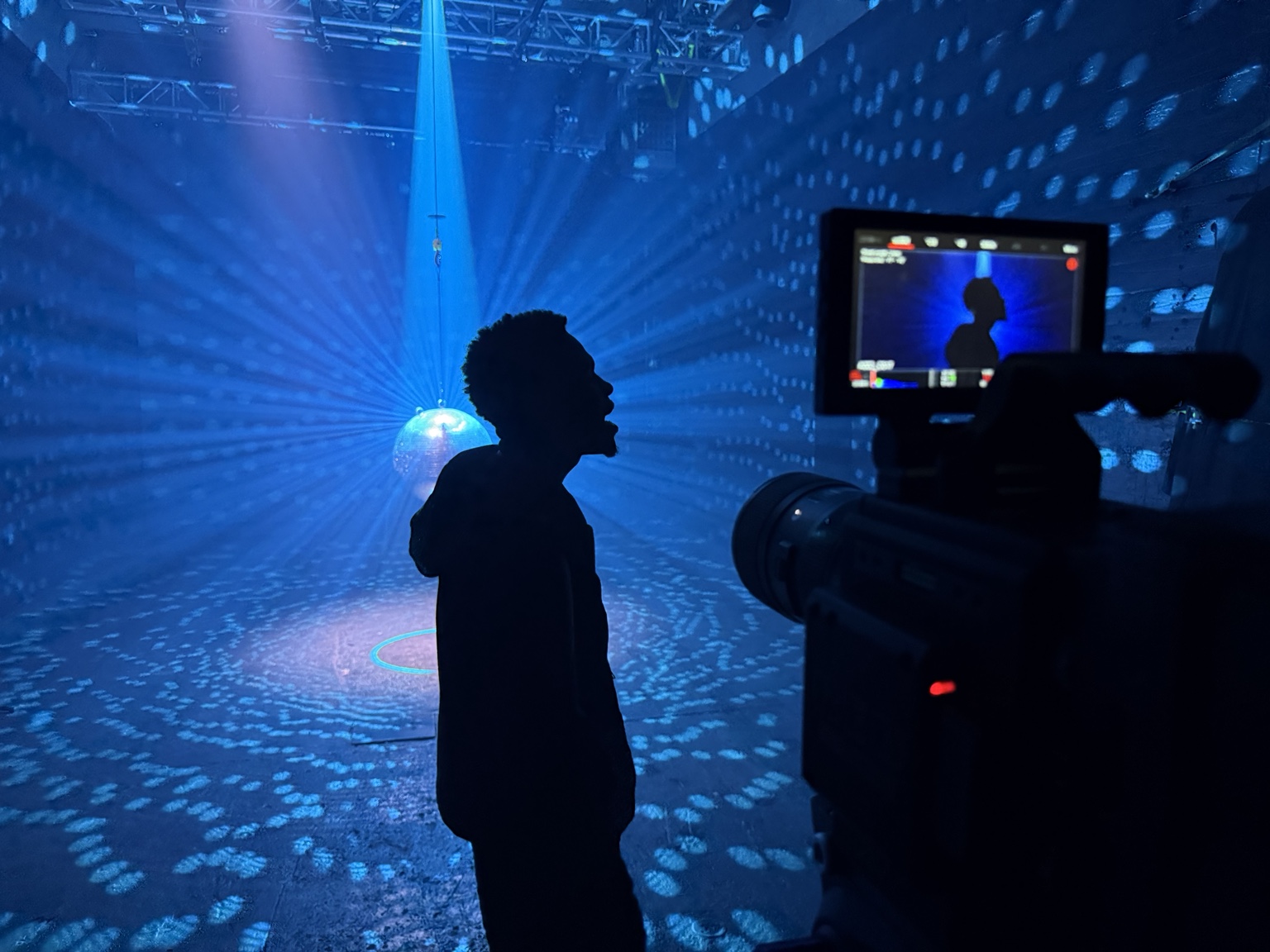 Blue lighting and mirrored reflections on a music video set, with a camera in the foreground