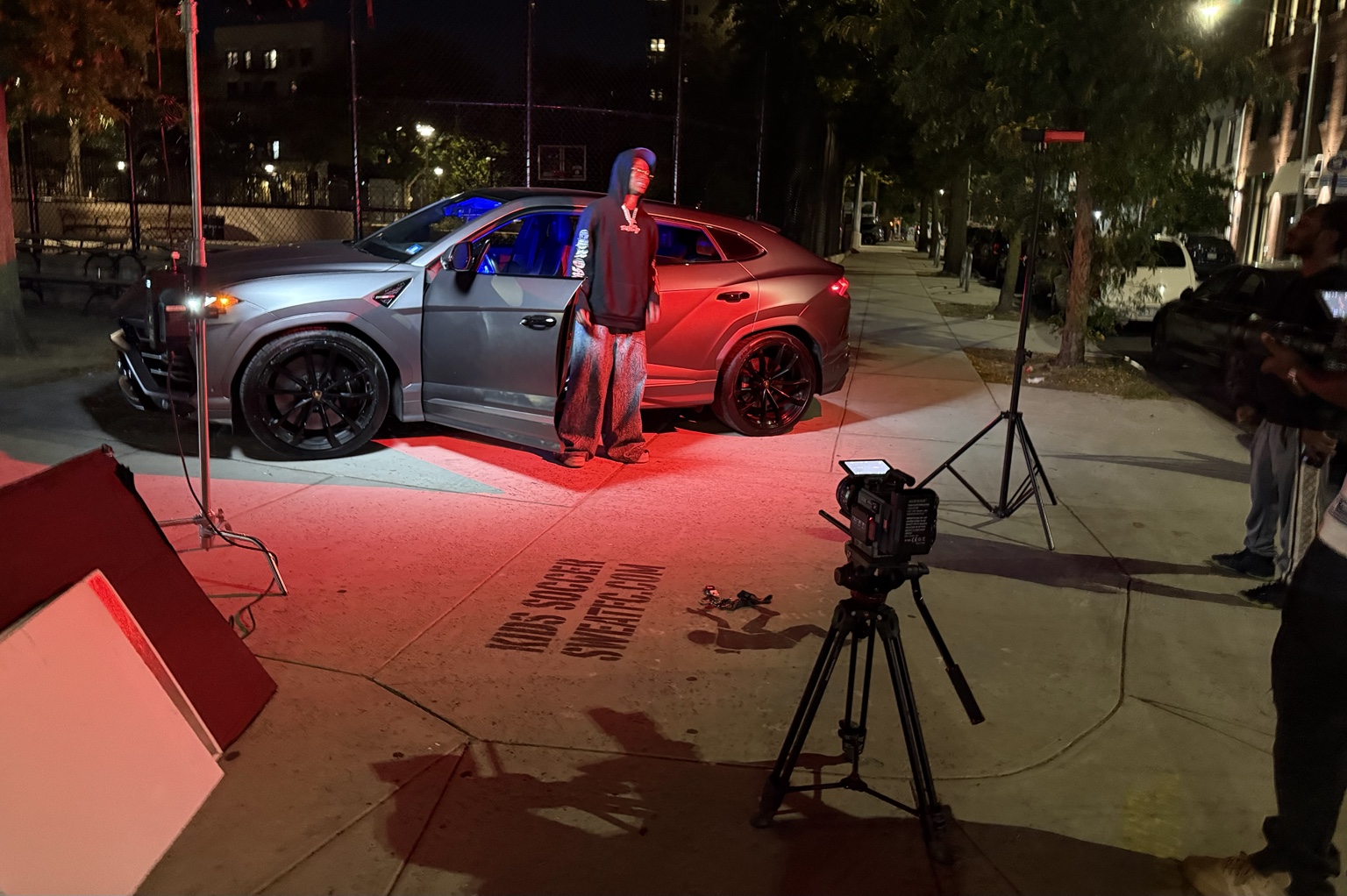 Night music video shoot with an artist, vehicle, camera, and red lighting